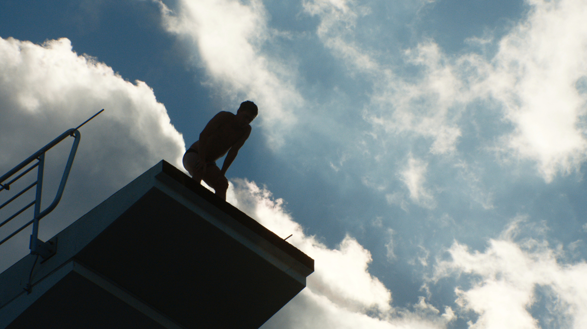 male diver peering over edge of diving board, silhouetted against the sky