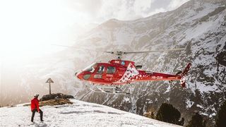 A red rescue helicopter arriving on a snowy summit