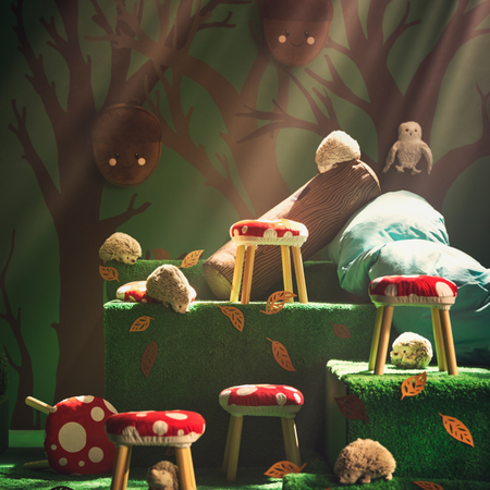 a grassy platform featuring five ikea toadstool stools. There is a log cushion, hedgehog and acorn soft toys.