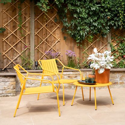 A patio with a bright yellow garden chair set with a matching table