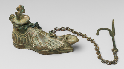 a bronze oil lamp shaped like a foot with a hanging chain