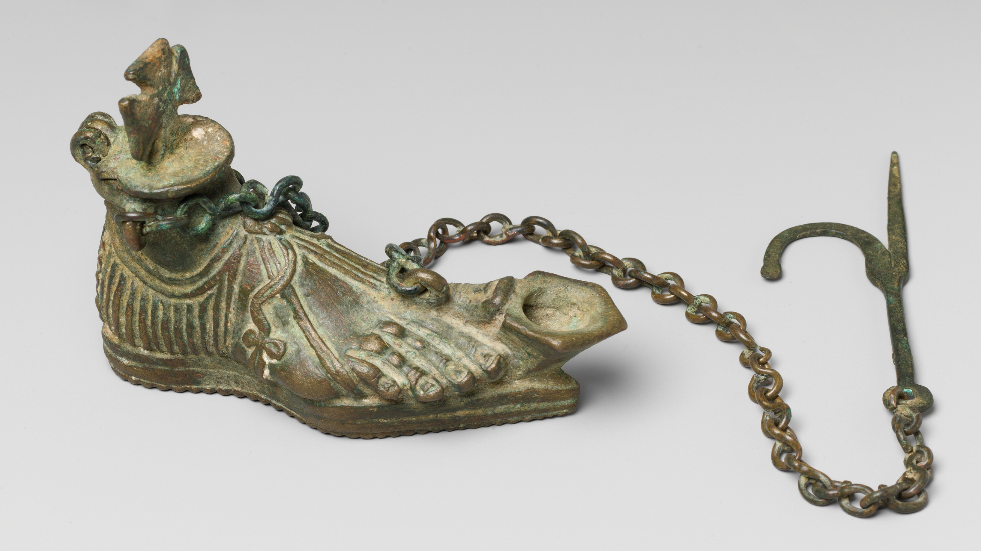 a bronze oil lamp shaped like a foot with a hanging chain