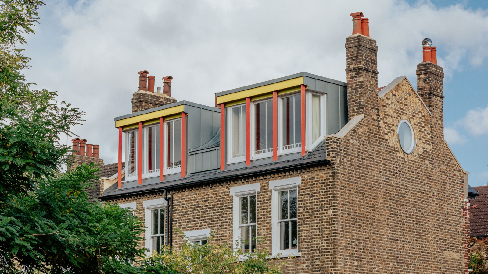 large brick house with double dormer loft windows in grey cladding with yellow fascia and red decorative columns