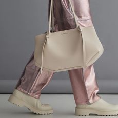 A tan Charles & Keith bag hanging by pink metallic trousers and tan boots