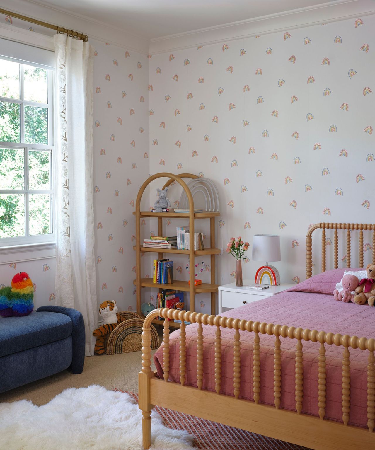 A kid's bedroom with a wooden bed frame and rainbow-patterned wallpaper