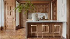 An all wood panelled kitchen with matching doors and floor, white walls, and a marble countertop