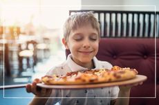 Child in restaurant holding a delicious pizza up to his face to enjoy the aroma