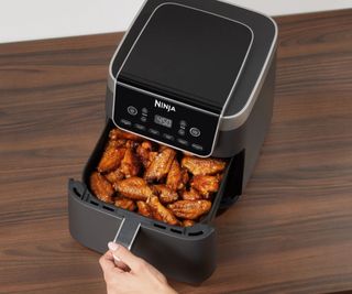 Ninja Air Fryer on a wooden table with the drawer pulled open, full of chicken wings