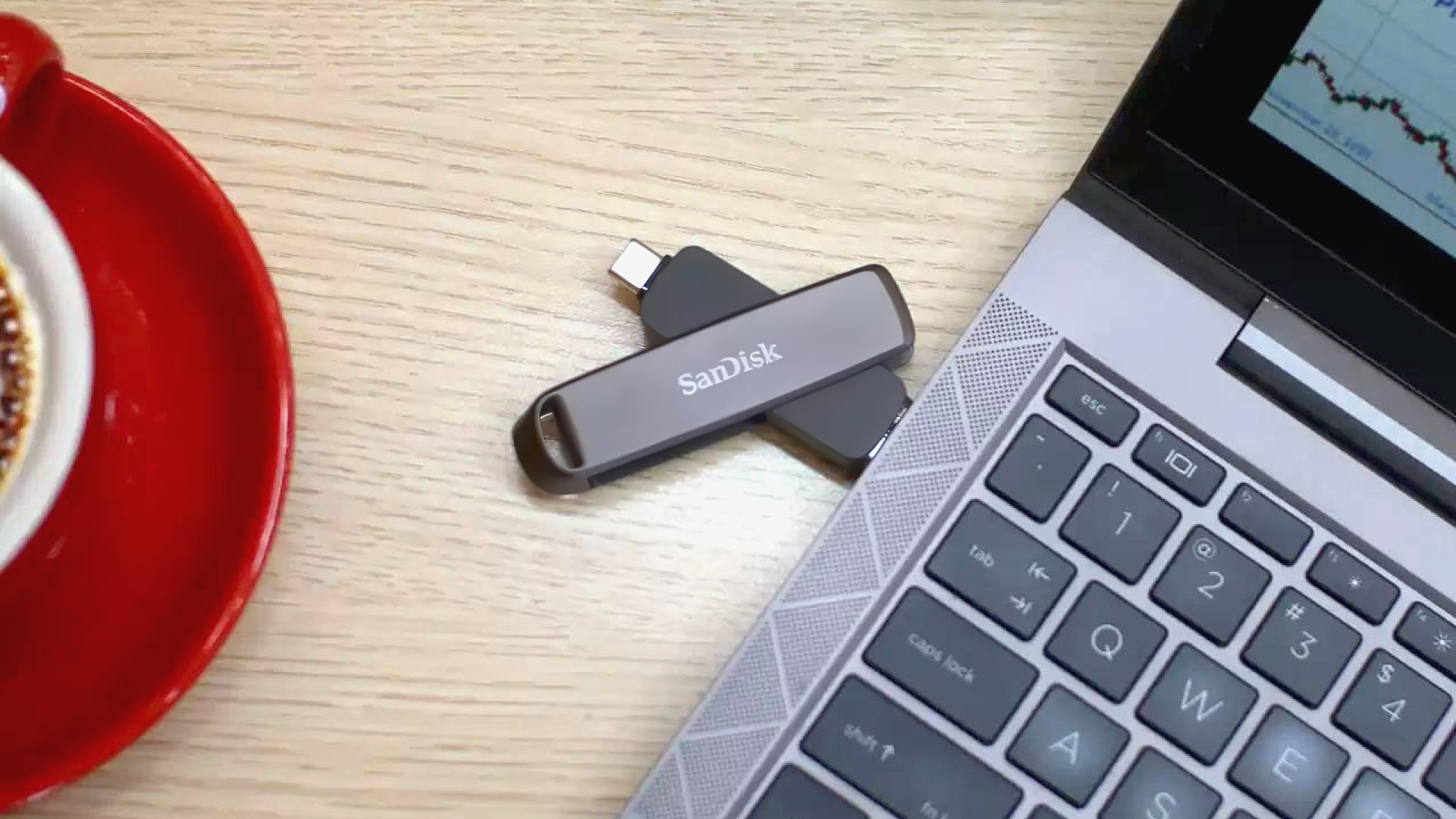 A promotional image of a SanDisk Extreme Pro Dual USB drive, shown inserted in the side of a laptop resting on a desk