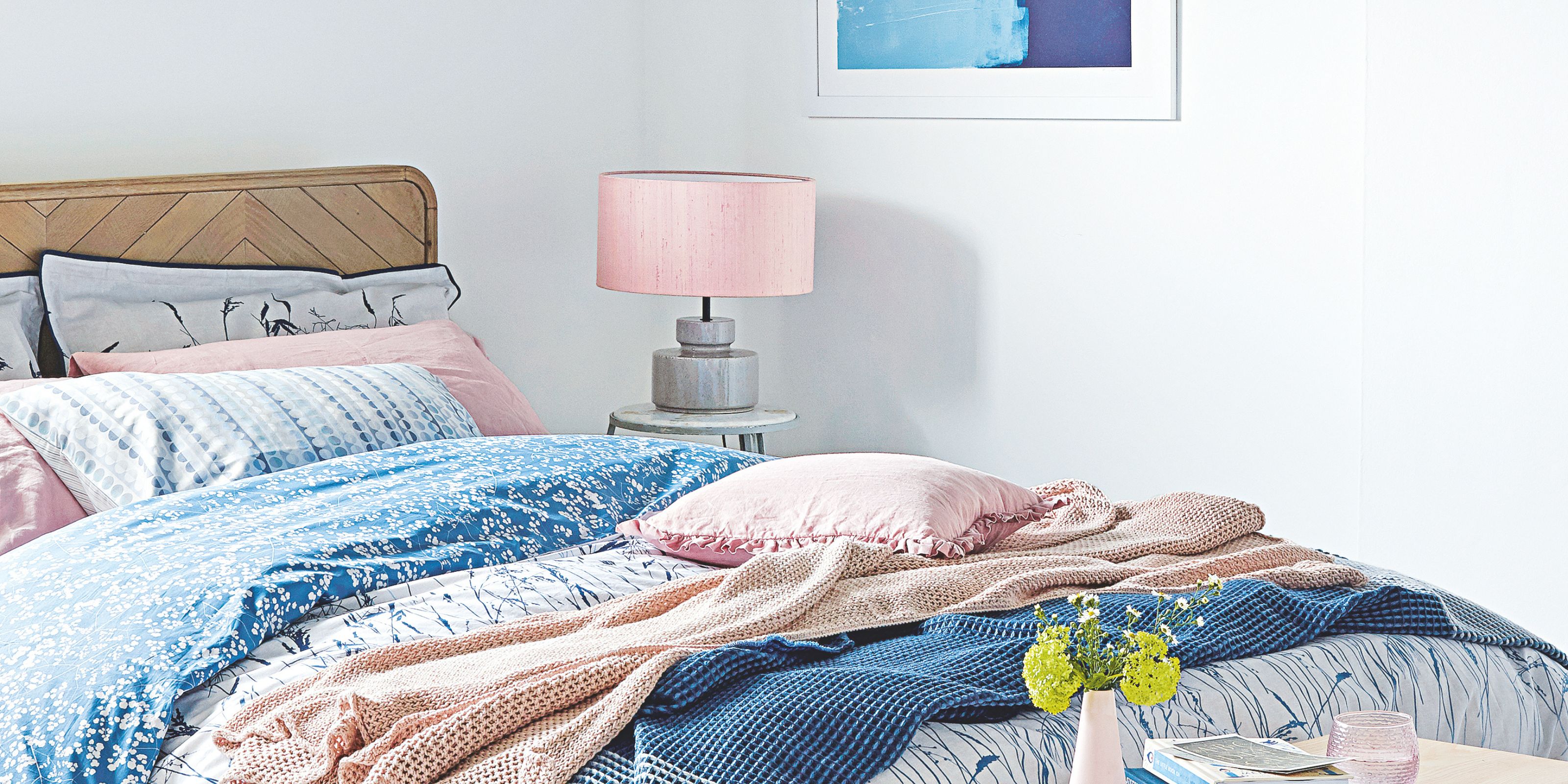 A bedroom with white walls, pink lamp and wooden bedframe, with pink and blue bed sheets
