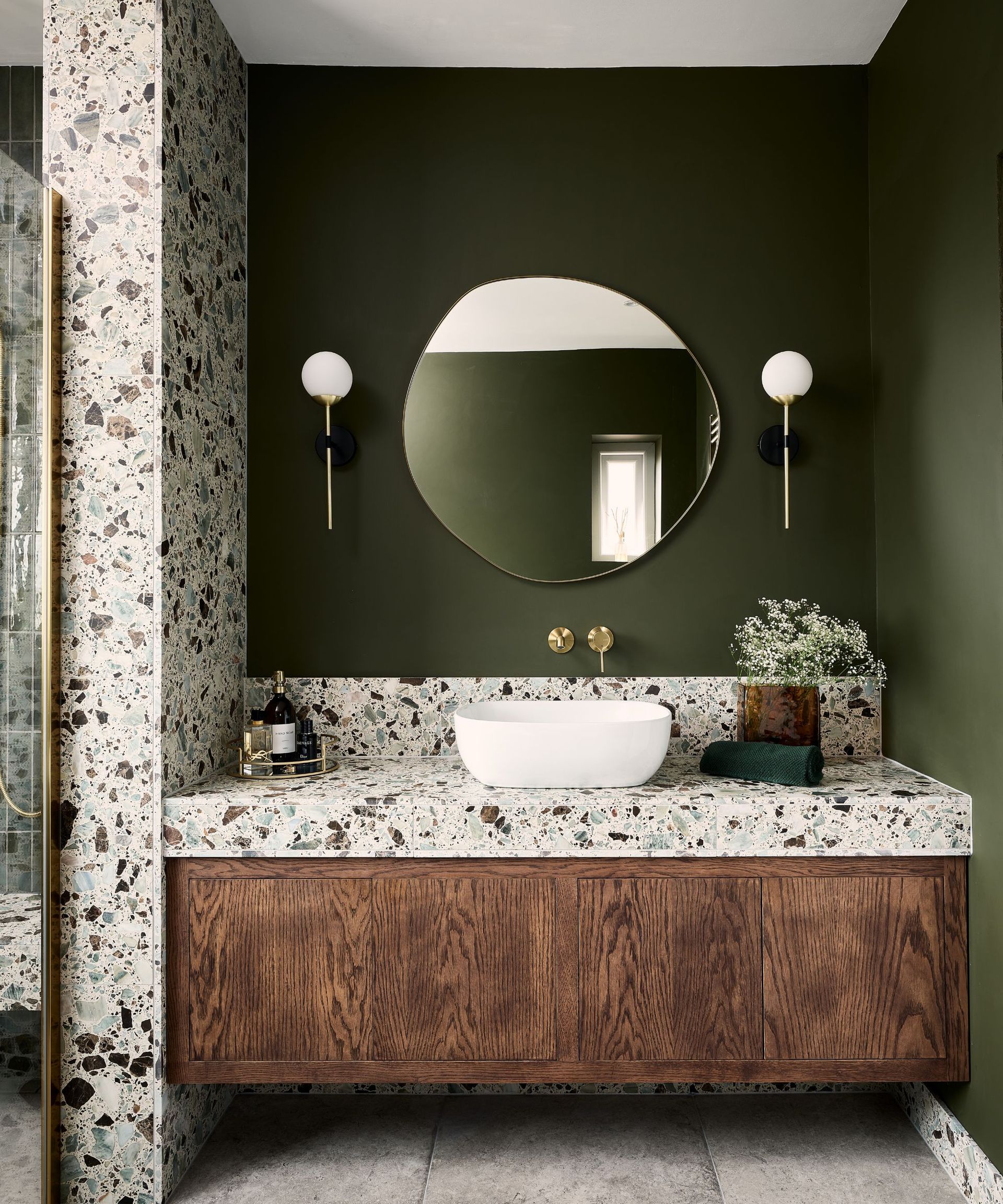 A retro bathroom with dark green walls, terrazzo walls, and terrazzo countertop and a wooden vanity