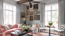 a traditional living room with a large pink couch, a coffee table with books and a vase of flowers, a floral accent chair, and a cluster of art hung in the corner of the room