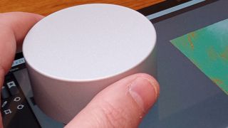 Microsoft Surface Dial; a small cylindrical gadget us held between fingers and a thumb