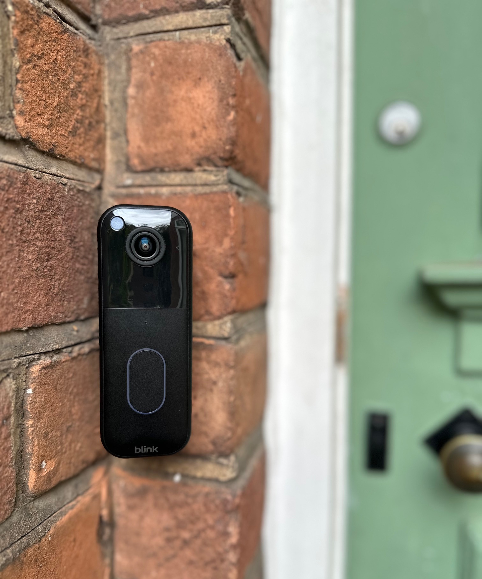 Black Blink video doorbell attached to outside wall next to green door