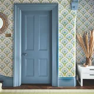 A blue wooden door surrounded by large scale print green blue and cream wallpaper