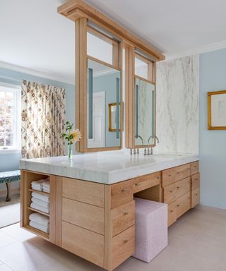 pale blue bathroom with wooden dresser and double mirrors