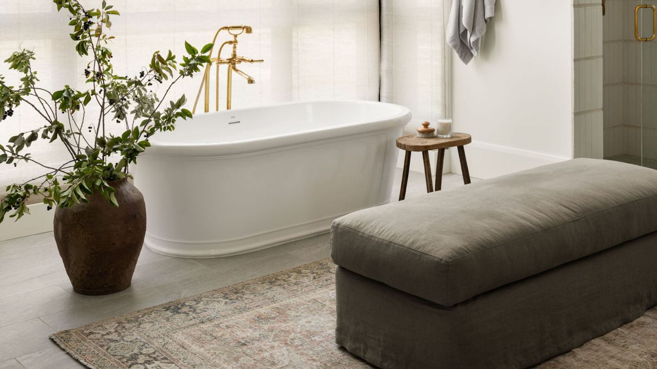 bathroom with tub, rug, ottoman, stool, and vase filled with large foliage