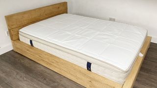 The DreamCloud Luxury Hybrid mattress review: Image shows the mattress placed on a light wooden frame in our reviewer's house during testing