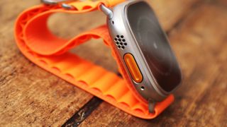 Apple Watch Ultra med oransje rem på et trebord.