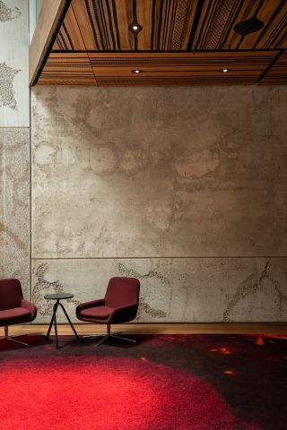 Interior room with a neutral colour marble effect stone wall, wood flooring, red patterned rug, two dark red sitting swivel chairs on silver metal stands, small round side table in the middle of the chairs