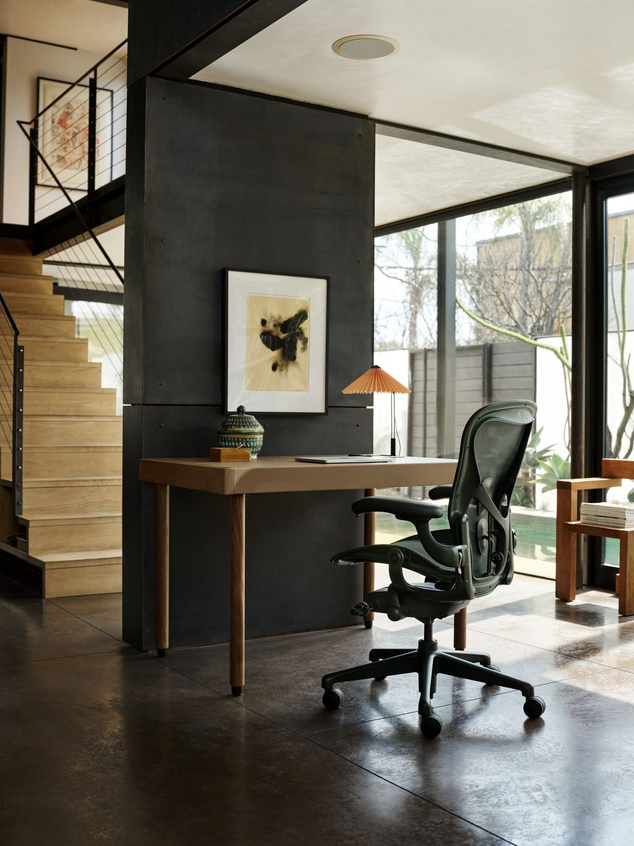 Image of the Herman Miller Jasper chair in green at a beige desk in a very modern house with lots of windows, black walls, and black stone flooring.