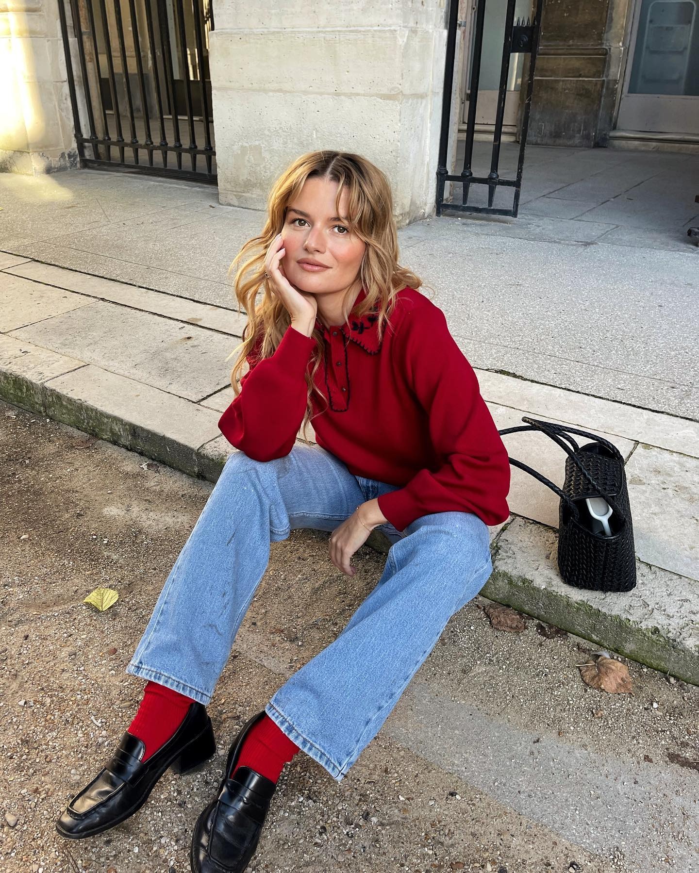 Woman wears a red sweater, 90s style jeans, red socks and black heeled loafers.