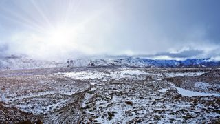 High angle aerial shot of an icy rocky terrain with mountains in the distance.