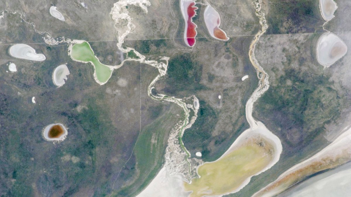 A satellite photo showing a pair of rivers and a series of colorful lakes surrounding a giant white expanse