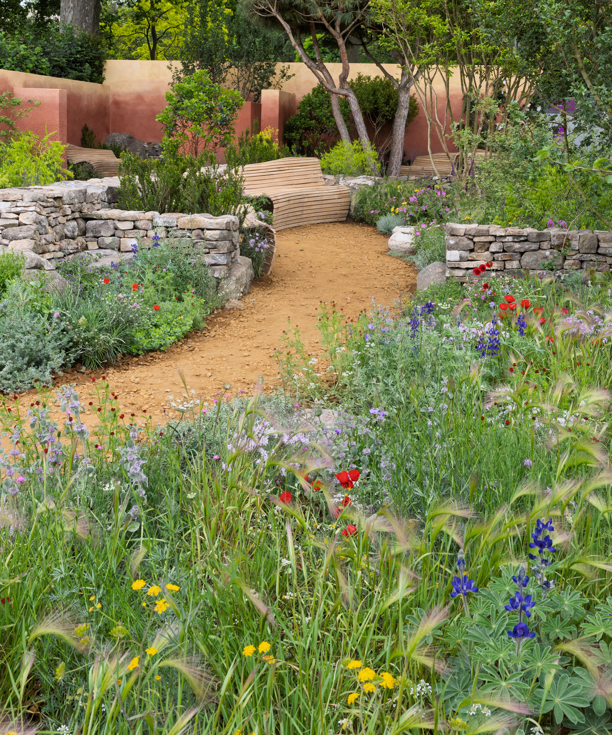 naturalistic garden design with curved beds and a curved path, with brick walls and a garden bench