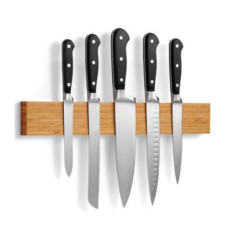 A wooden wall knife block with five knives with black handles on it