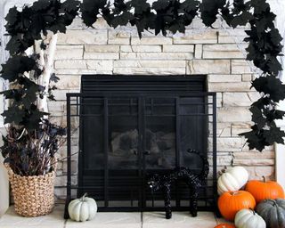 A white brick fireplace with a black bat garland on top of it and pumpkins below it