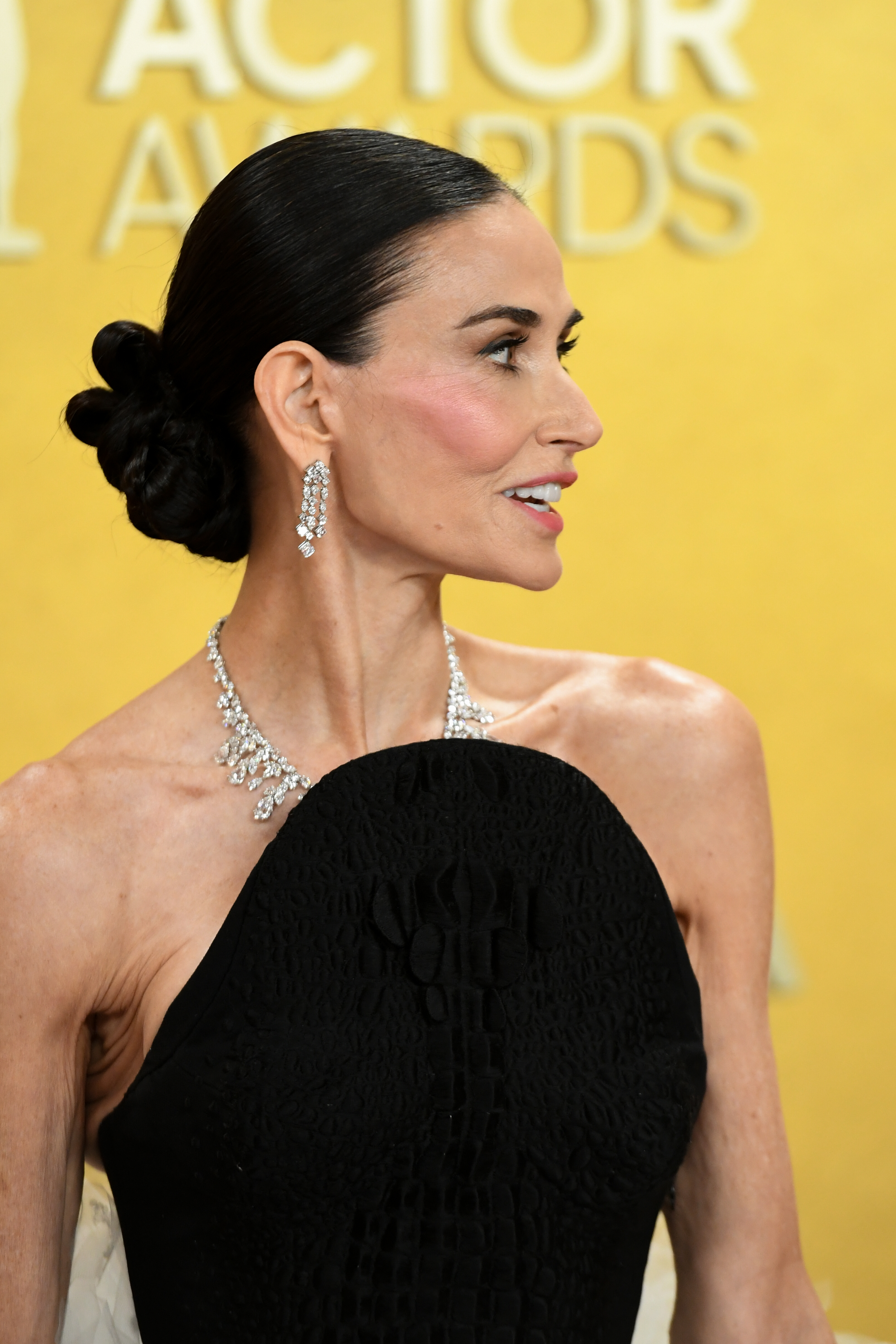 a white woman with dark wears her hair pulled back into a sleek bun and poses on a red carpet