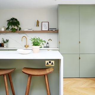 Kitchen with pale green cabinetry and island with white marble wrap top