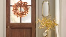Fall wreath on inside of wooden door with yellow faux flowers in a white vase beside it