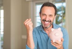 a happy man celebrating while holding a piggy bank