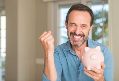 a happy man celebrating while holding a piggy bank