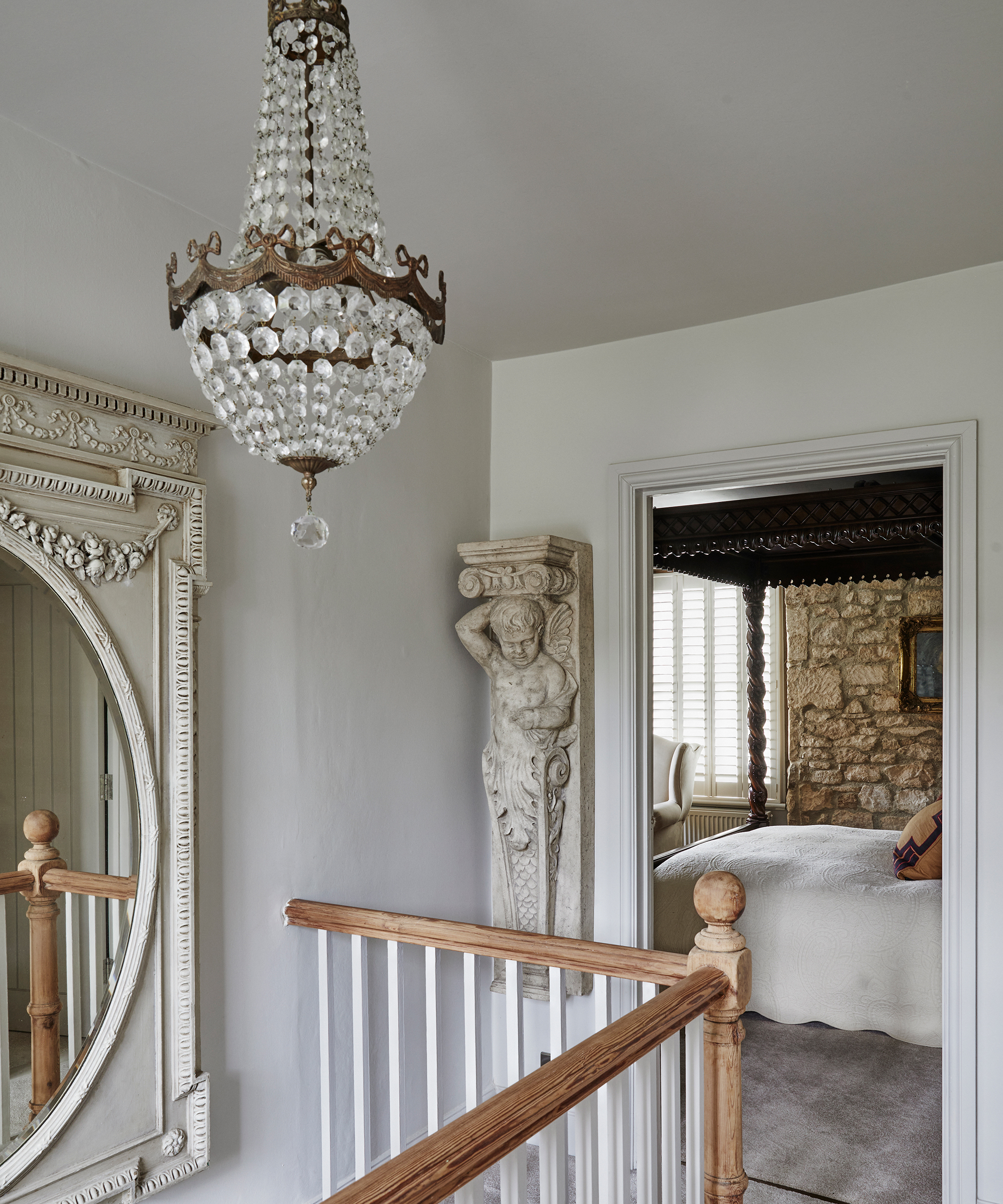 View from a landing with an antique crystal chandelier and stone cherub to bedroom with mahogany four-poster bed