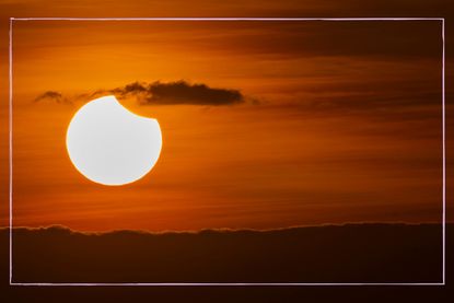 a photo of the sky during sunrise showing a partial solar eclipse
