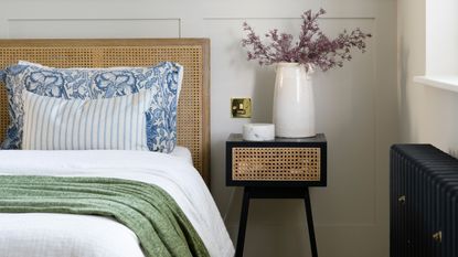 A bedroom featuring a rattan headboard, rattan side table and green, white and blue bedding