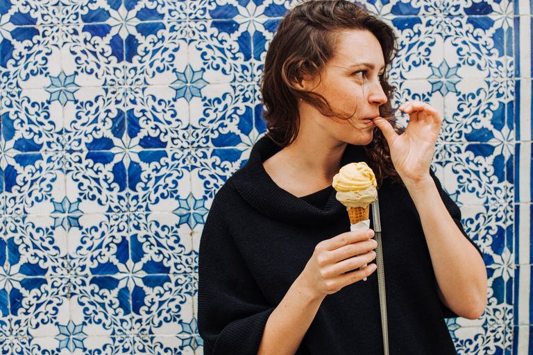 Millennial woman licking finger while eating ice cream at a tiled wall, destinations for solo travel