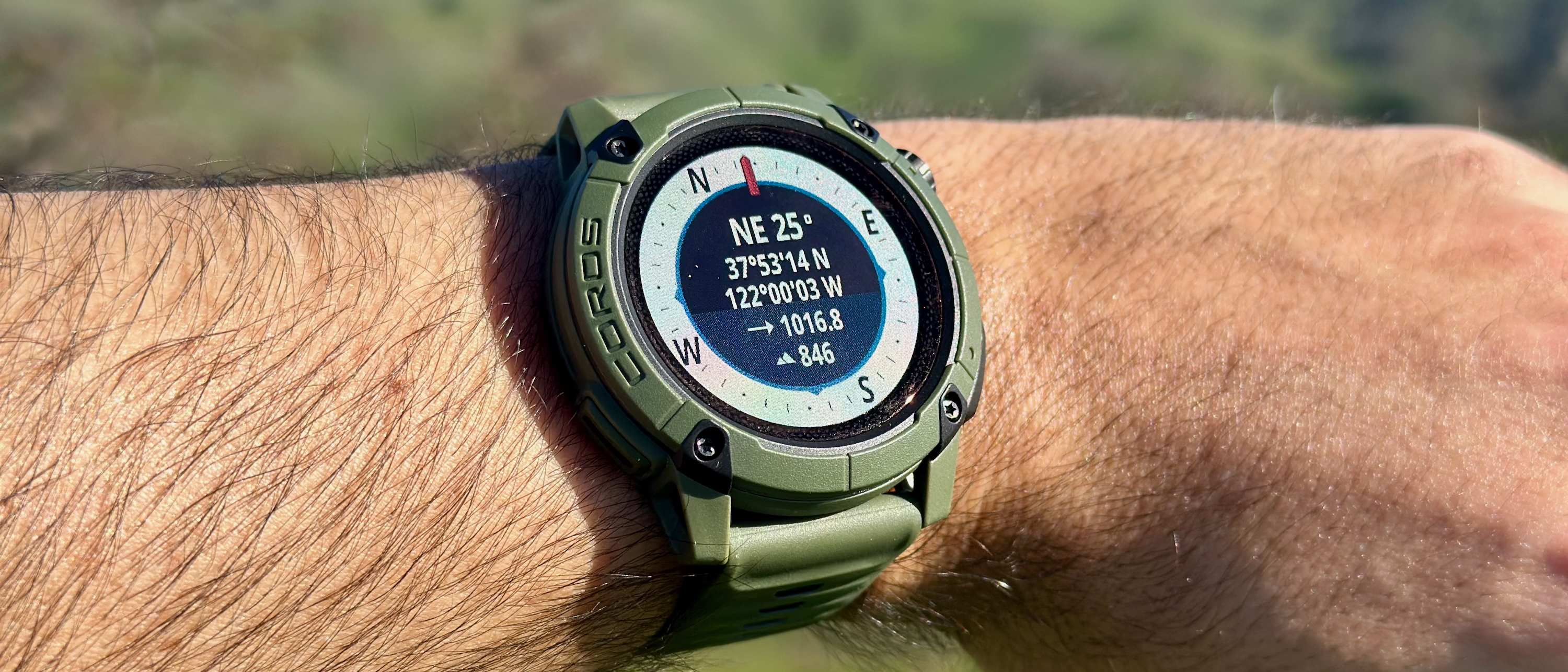 A photo close-up of the COROS NOMAD smartwatch, showing the Compass app with current latitude, longitude, and direction.