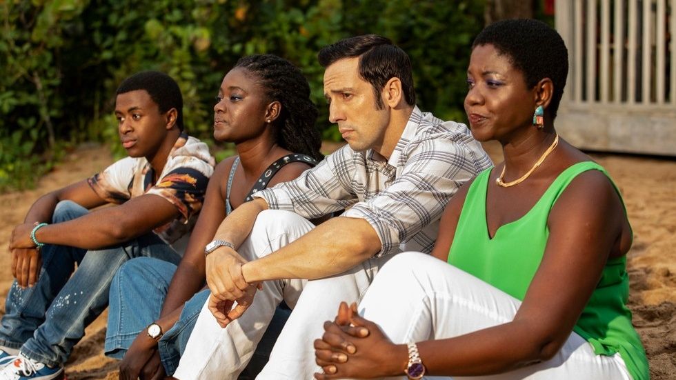 The cast of Death in Paradise sit on the beach looking out to sea