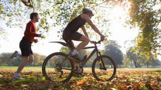 Cyclist riding mountain bike with jogger following 