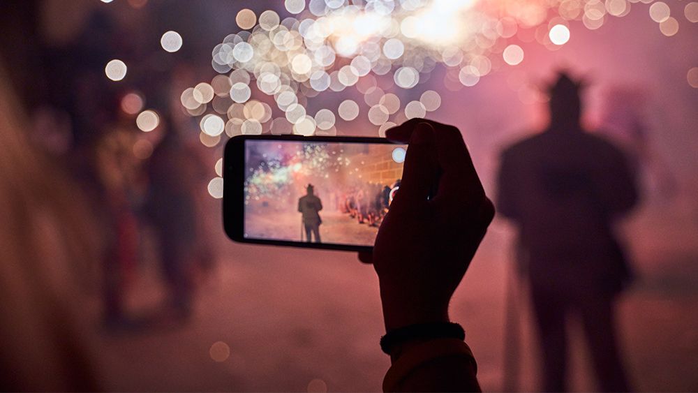 A photo of someone taking a photo of fireworks on a phone