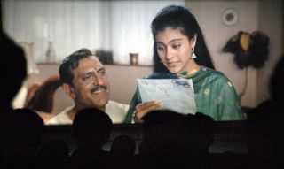 a man and a woman smiling and holding a letter on a screen in Dilwale Dulhania Le Jayenge (1995)