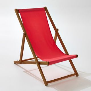 A traditional fold out wooden deckchair with red material seat.