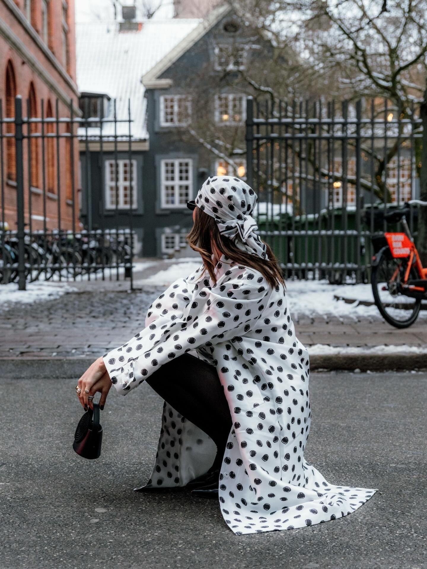 Woman wears white and black polka-dot dalmatian style coat, head wrap, and black tights.