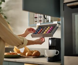 female hands pulling down coffee pod storage unit from below wall mounted kitchen cabinet