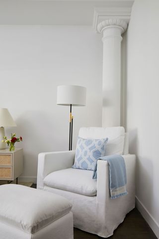 Corner of a room with white accent chair and matching stool, architectural pillar behind