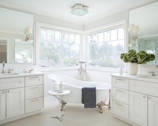 A white bathroom with a freestanding tub in front of a double corner window